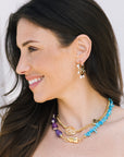 Woman wearing gold hoop earrings and colorful necklaces against a white background