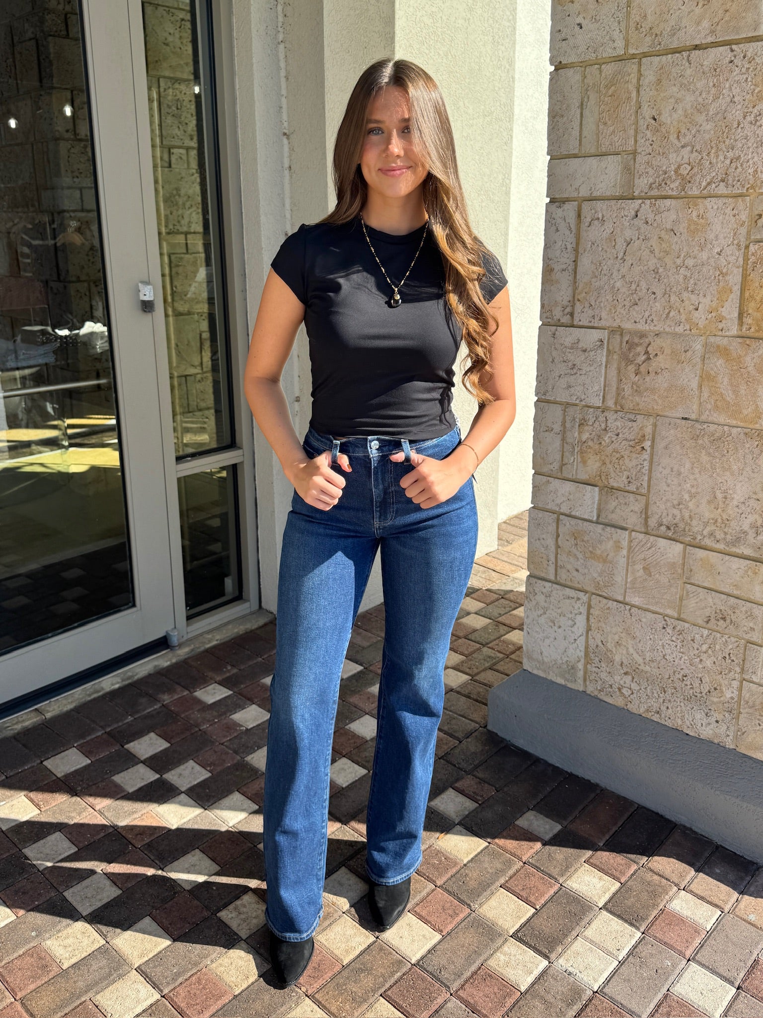 Woman wearing a black top and blue jeans standing on a patterned pavement.