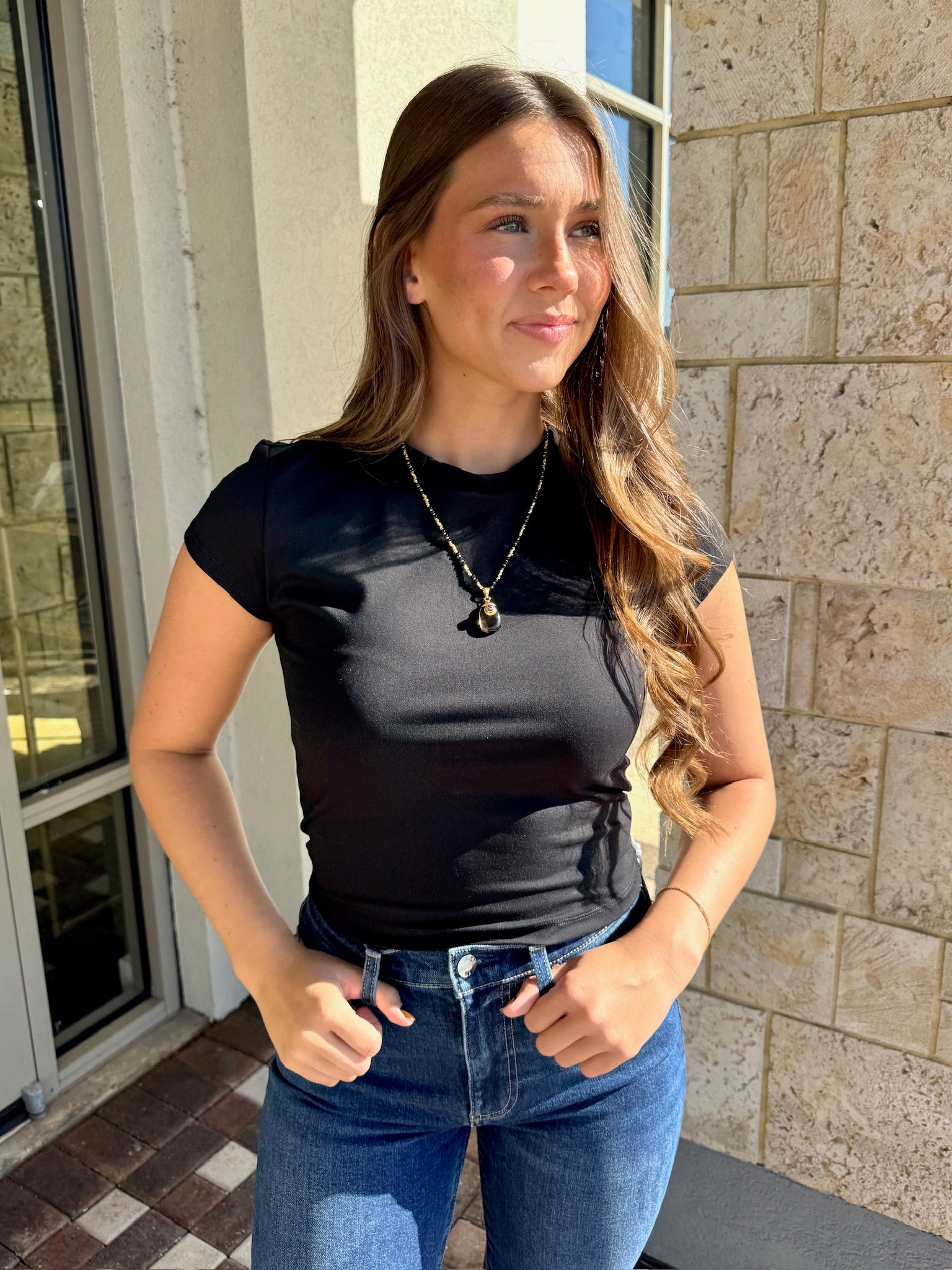 Woman wearing a black top and blue jeans standing outside a building.