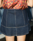 A person wearing a dark blue denim mini skirt with a red and yellow floral patterned top, shown from the back.