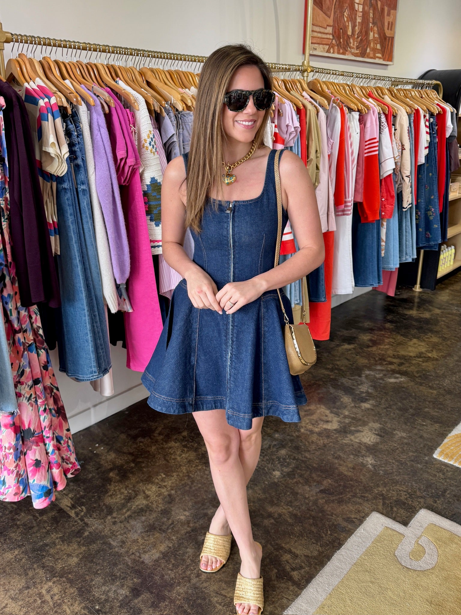Woman in a denim dress standing in a clothing store with racks of clothes in the background.