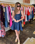 Woman in a denim dress standing in a clothing store with racks of clothes in the background.