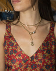 A close-up of a woman wearing a layered gold necklace with a small dangling charm, paired with a red and blue floral patterned top.