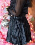 Person wearing a black outfit with a textured skirt against a festive background, side view