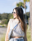 Woman wearing a white sequin top and denim pants outdoors with trees in the background