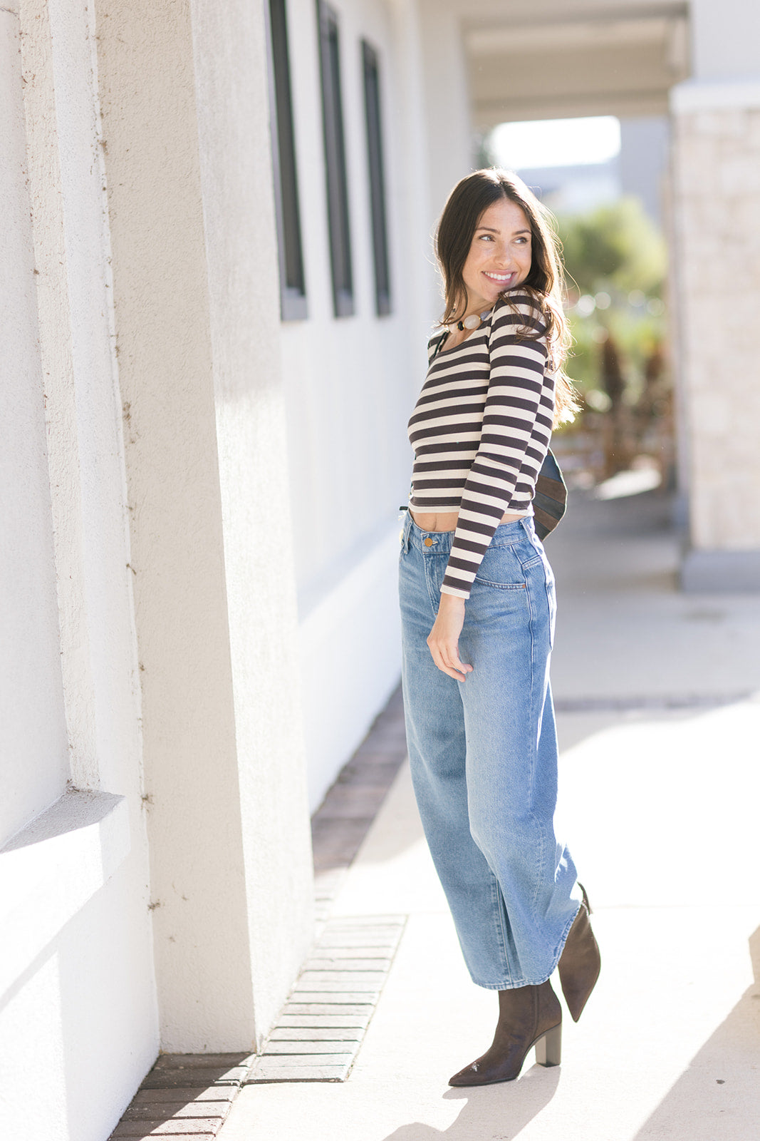 Woman wearing a striped shirt and jeans standing outdoors, looking over shoulder