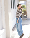 Woman wearing a striped shirt and jeans standing outdoors, looking over shoulder