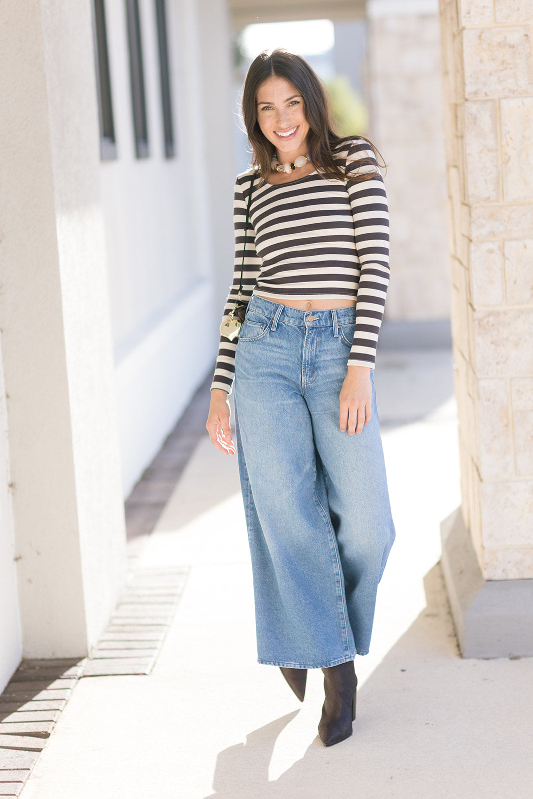 Woman wearing a striped shirt and wide-leg jeans standing outdoors.