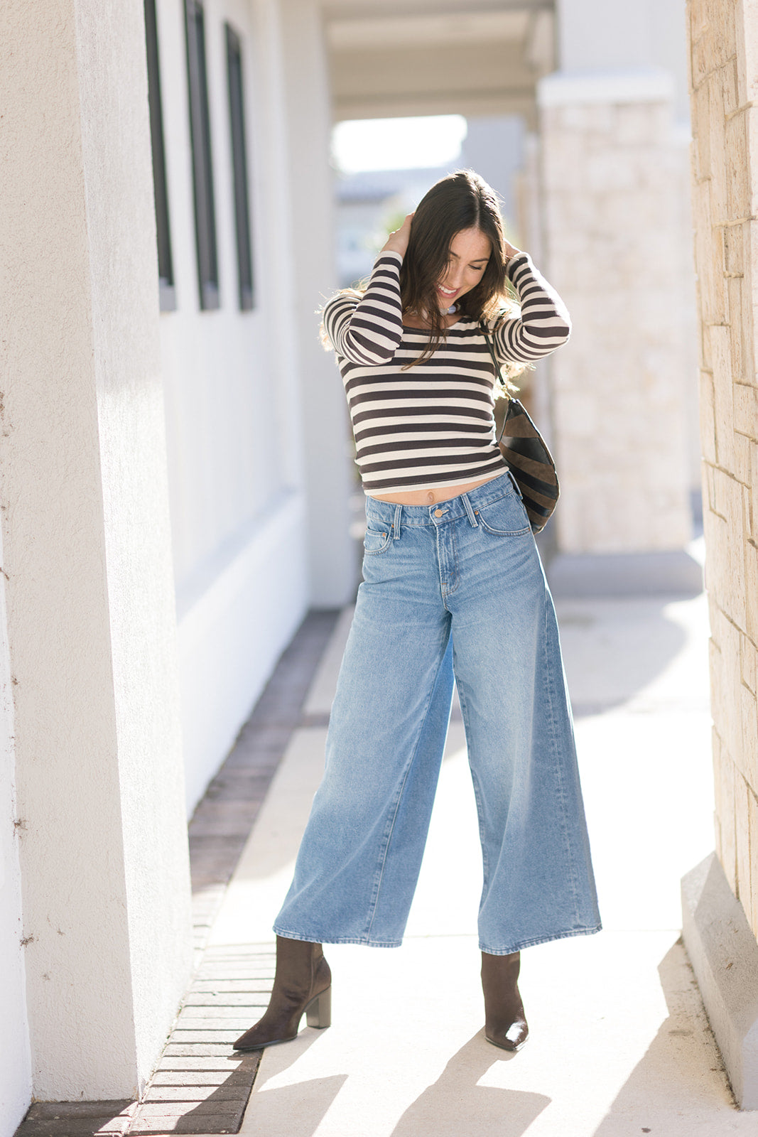 Person wearing a striped sweater and wide-leg jeans standing in a sunlit outdoor area.