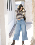 Person wearing a striped sweater and wide-leg jeans standing in a sunlit outdoor area.