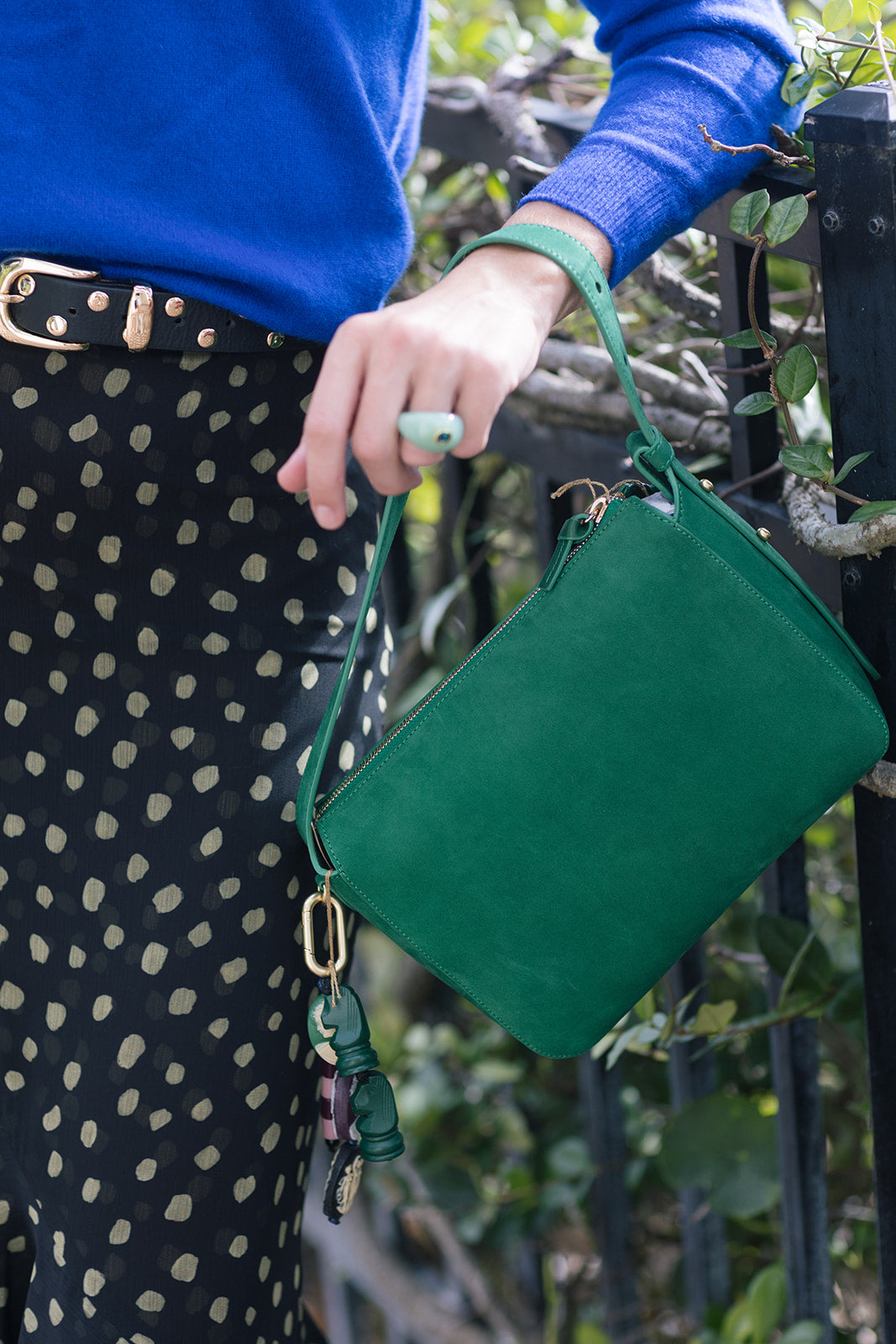 Green handbag with Cameo Fob held by a person wearing a blue sweater and polka dot skirt.