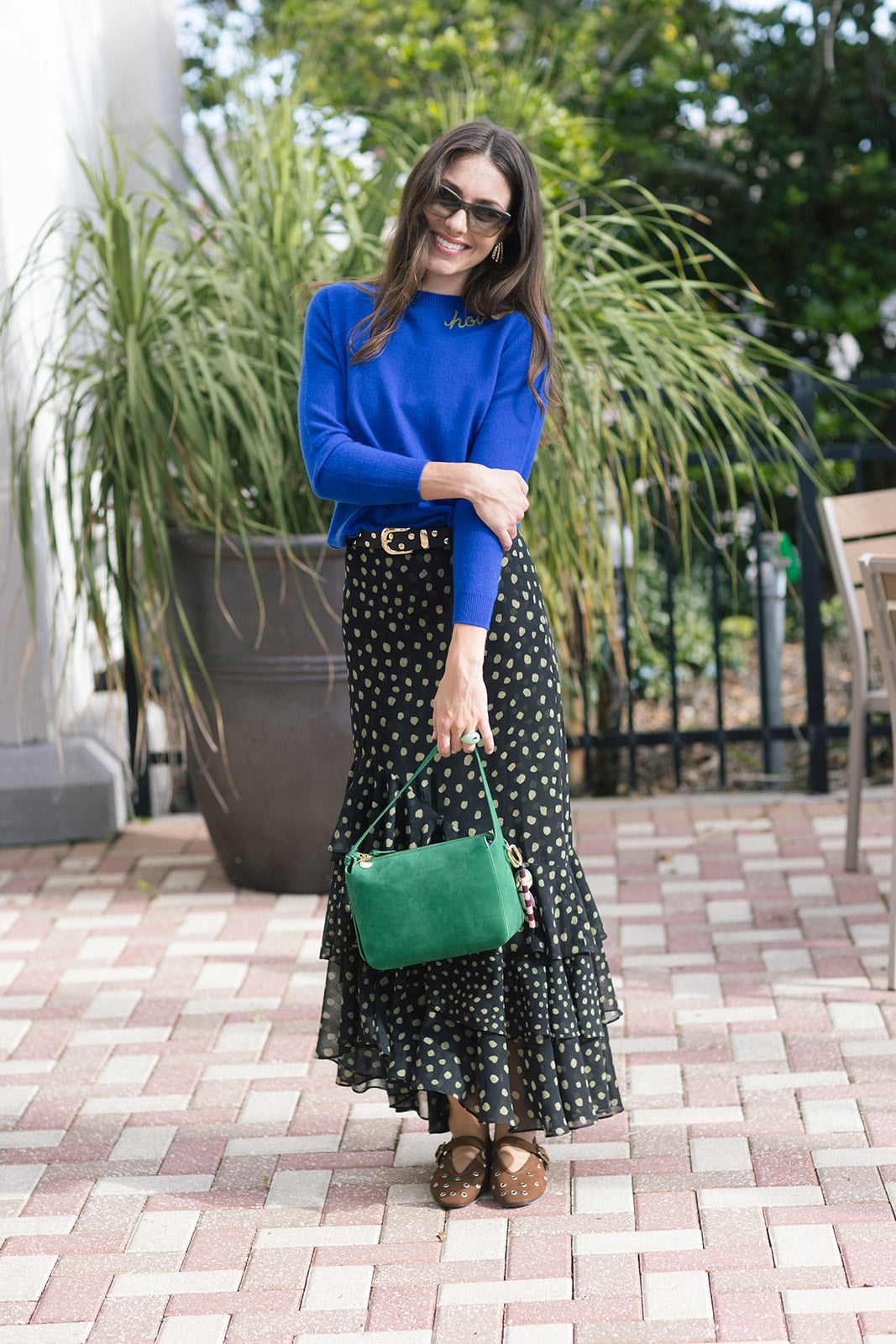 Woman in a blue sweater and polka dot skirt holding a green handbag outdoors.