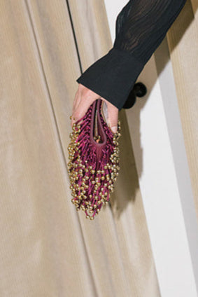 Hand holding a purple beaded clutch against a neutral background