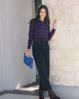 Woman in striped shirt and jeans holding a blue clutch against a stone wall, full body