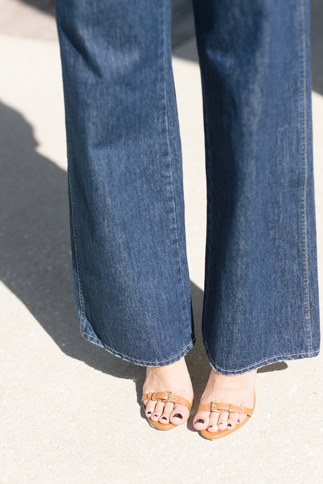 Close-up of blue jeans and brown sandals on a light background