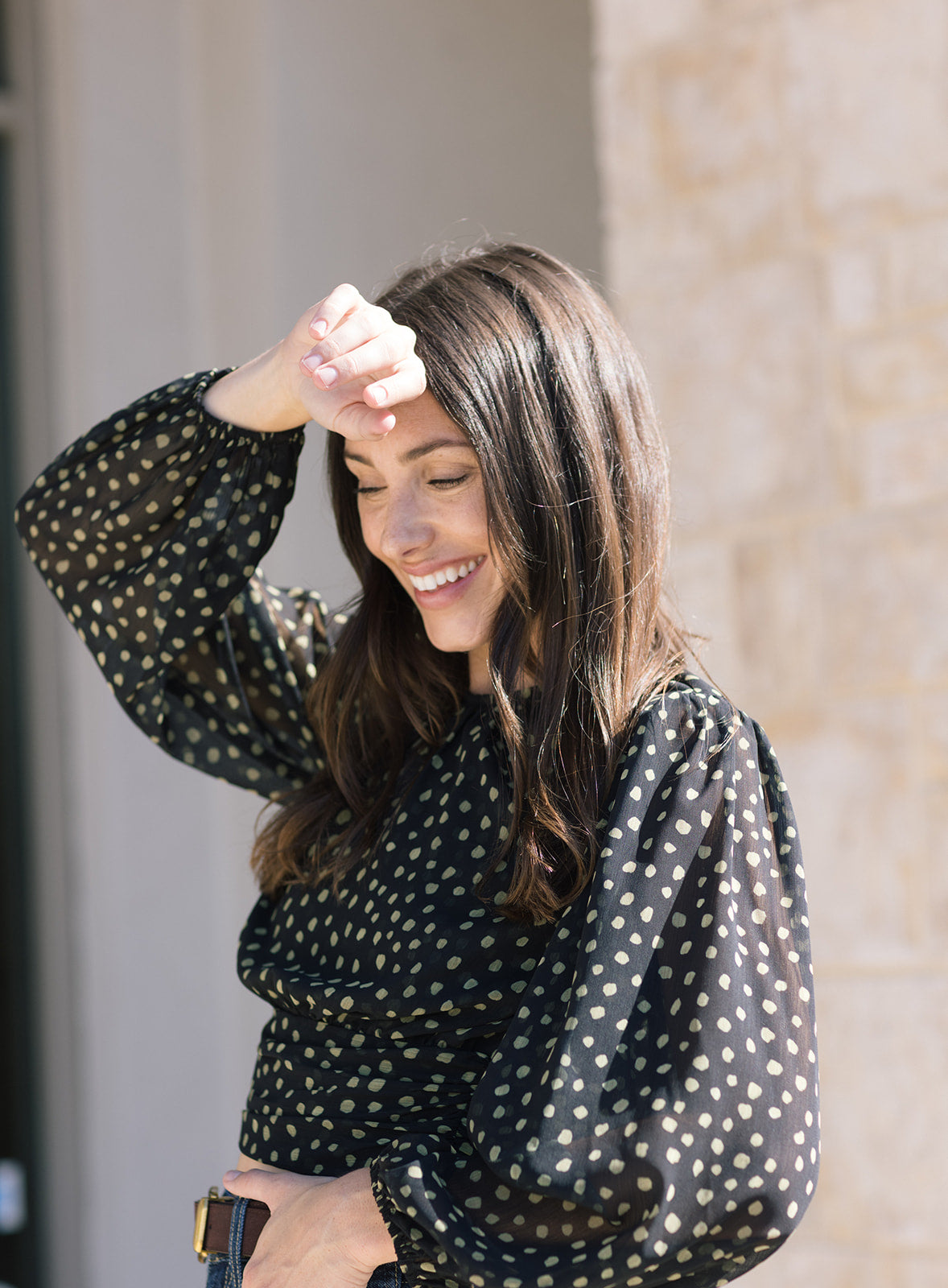 Woman wearing a black polka dot top with long sleeves, standing outdoors, front/side