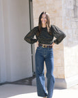 Woman wearing a black polka dot blouse and blue jeans standing outdoors.