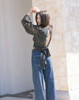 Woman wearing a polka dot blouse and blue jeans against a stone wall, back view