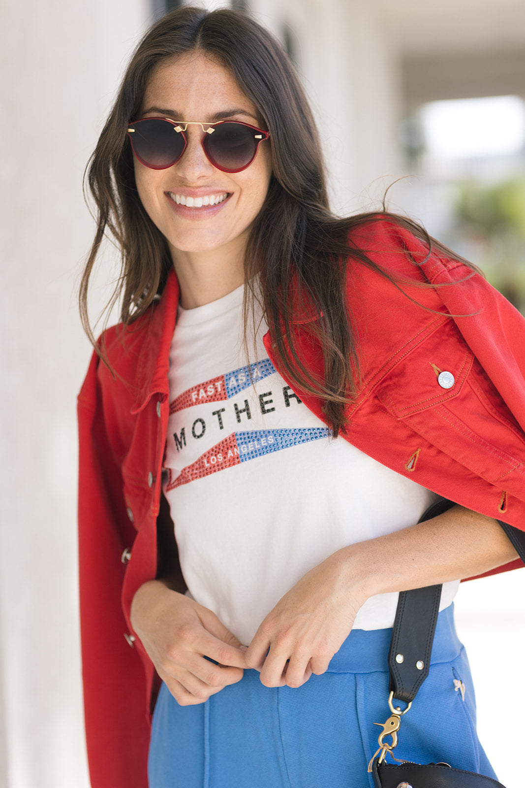 Woman wearing a red jacket, white t-shirt with text, and blue pants outdoors.