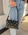 Person holding a black clutch with gold studs and 'Simon Miller' branding.
