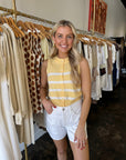 Woman in a yellow striped shirt and white shorts standing in a clothing store.