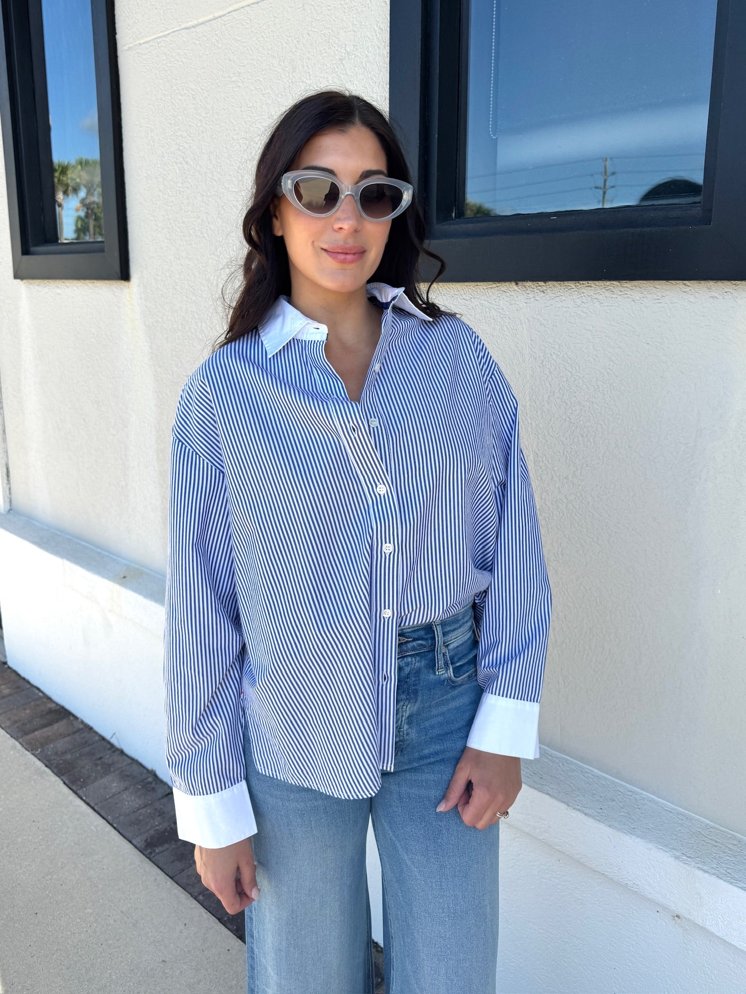 Woman wearing a blue and white striped shirt and sunglasses, standing in front of a building.