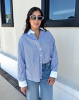 Woman wearing a blue and white striped shirt and sunglasses, standing in front of a building.