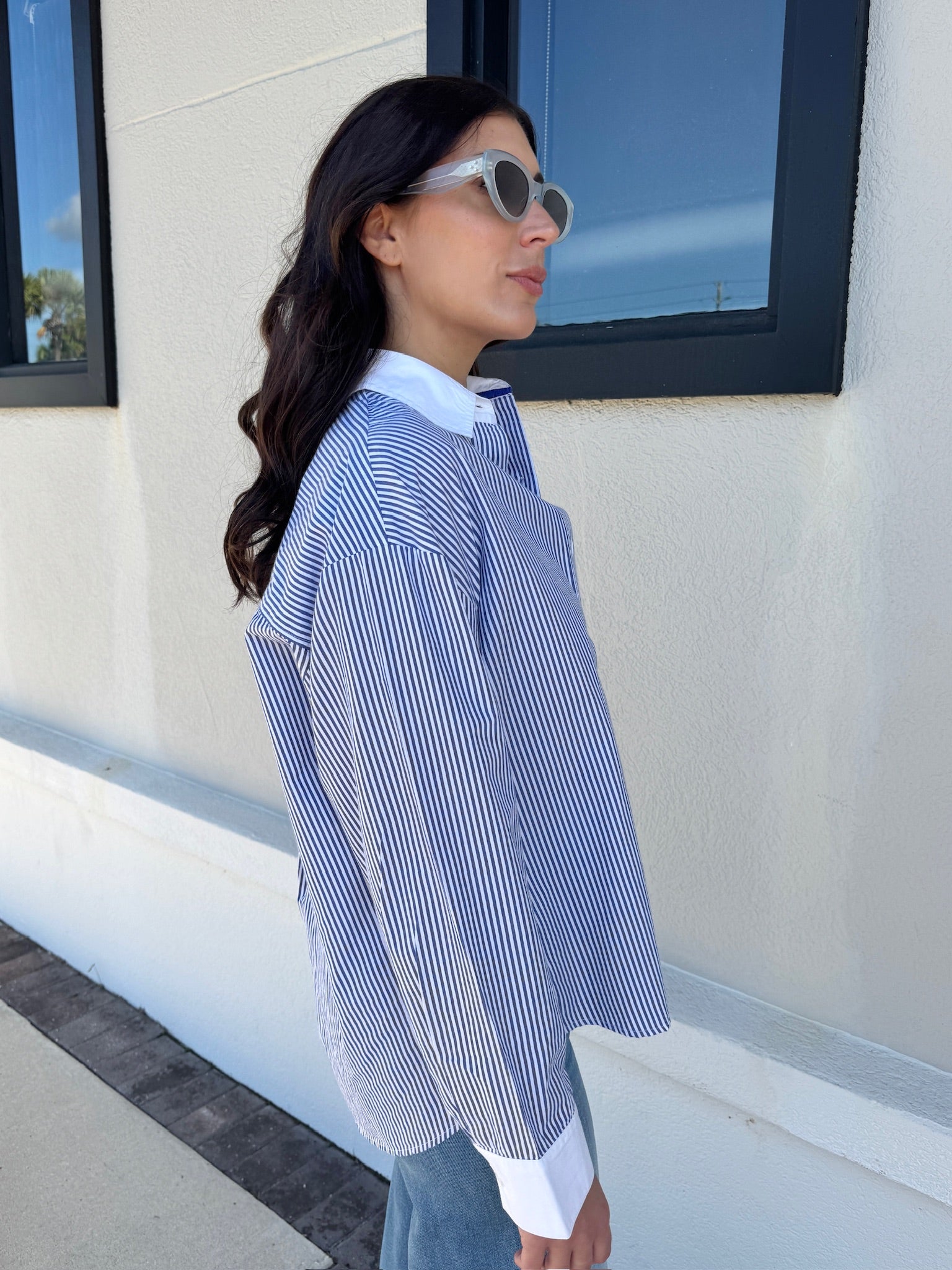 Woman wearing a blue and white striped shirt standing outside a building with large windows, side view