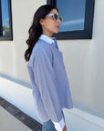 Woman wearing a blue and white striped shirt standing outside a building with large windows, side view