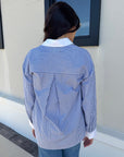 Person wearing a blue and white striped shirt with a collar, standing against a neutral wall. back view