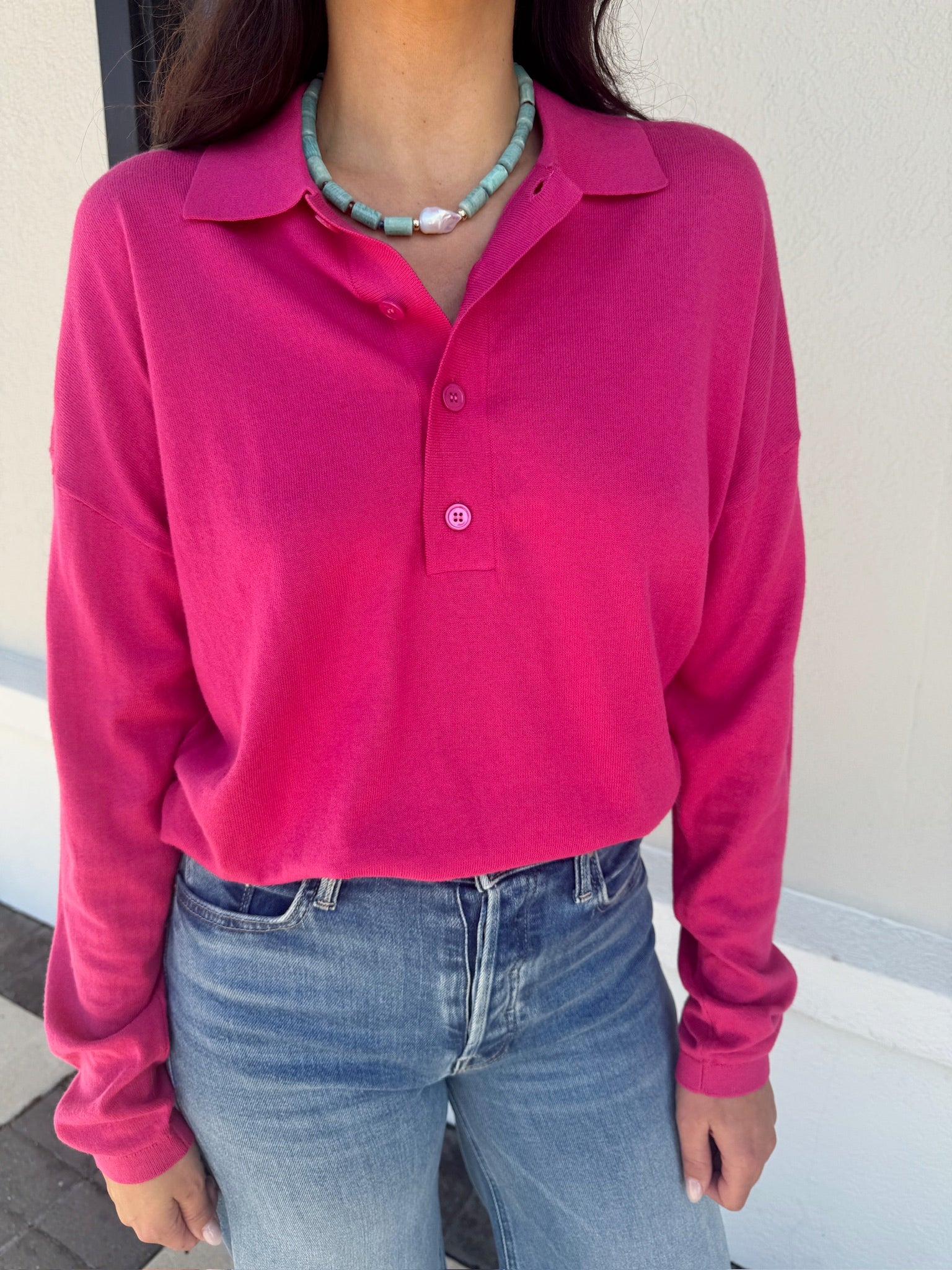 Person wearing a bright pink long-sleeve polo shirt and blue jeans, close up, top tucked in