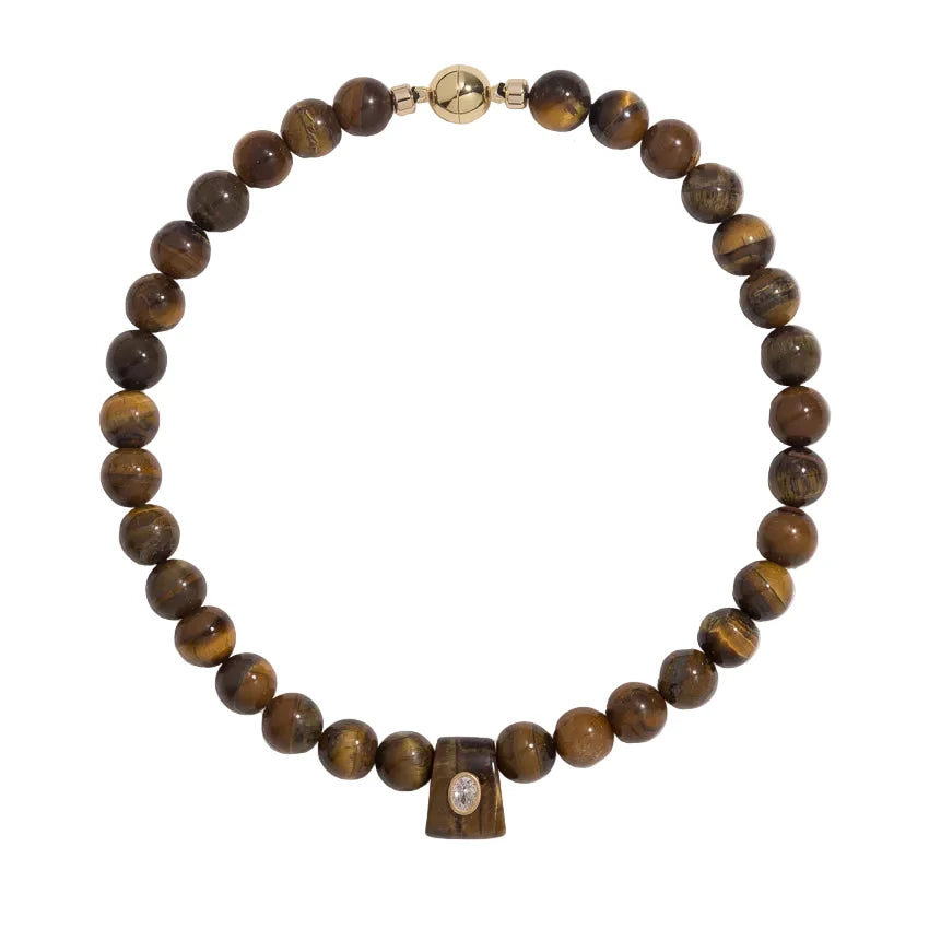 A beaded necklace made of polished brown tiger's eye beads, featuring a small gold-toned bead clasp at the top and a small rectangular wooden charm with a clear stone at the bottom center, shown on a plain white background.