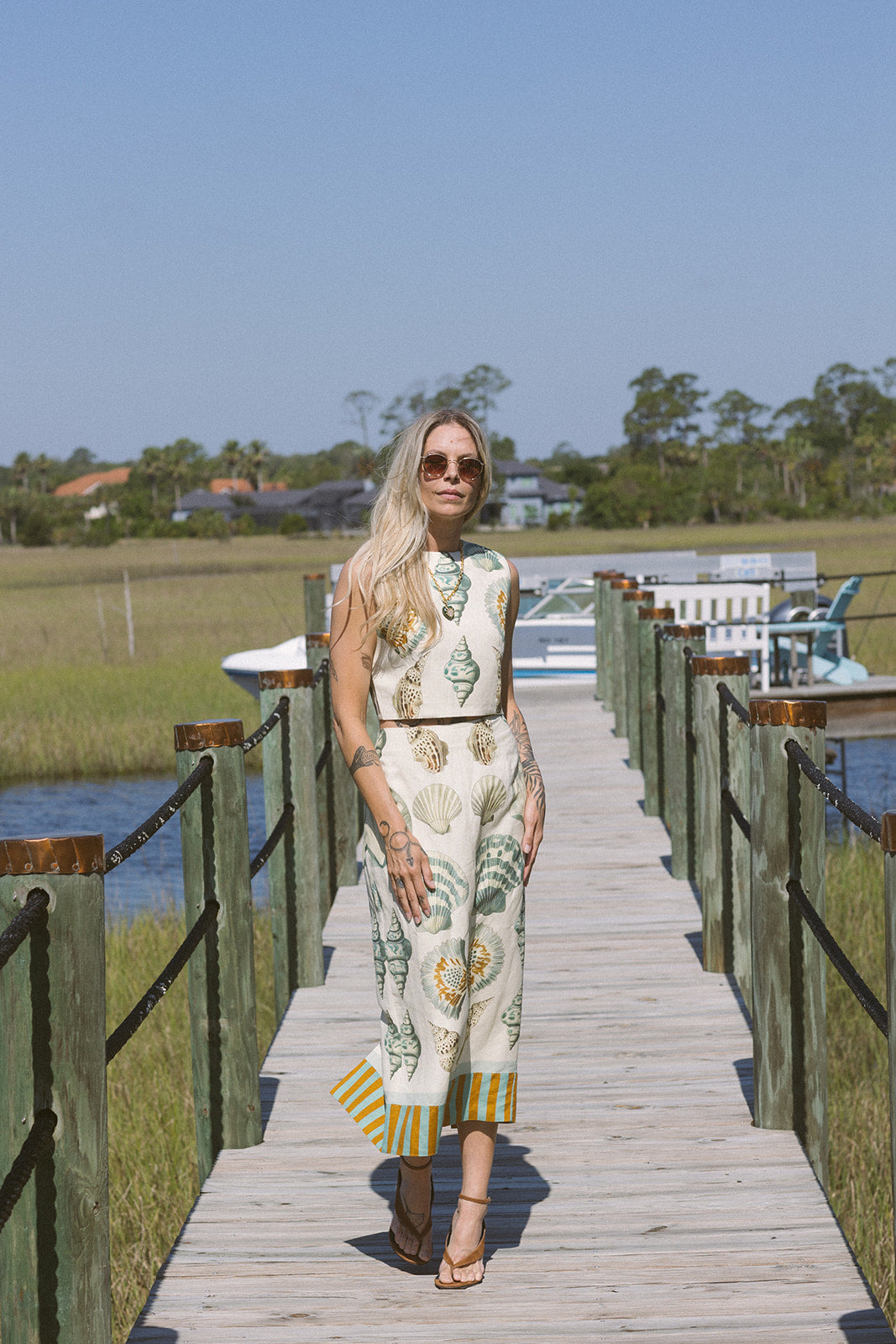 Woman in a patterned set standing on a wooden dock by a body of water.
