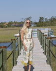 Woman in a patterned set standing on a wooden dock by a body of water.