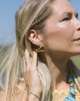 Woman wearing gold hoop earrings with a blue necklace against a clear sky.