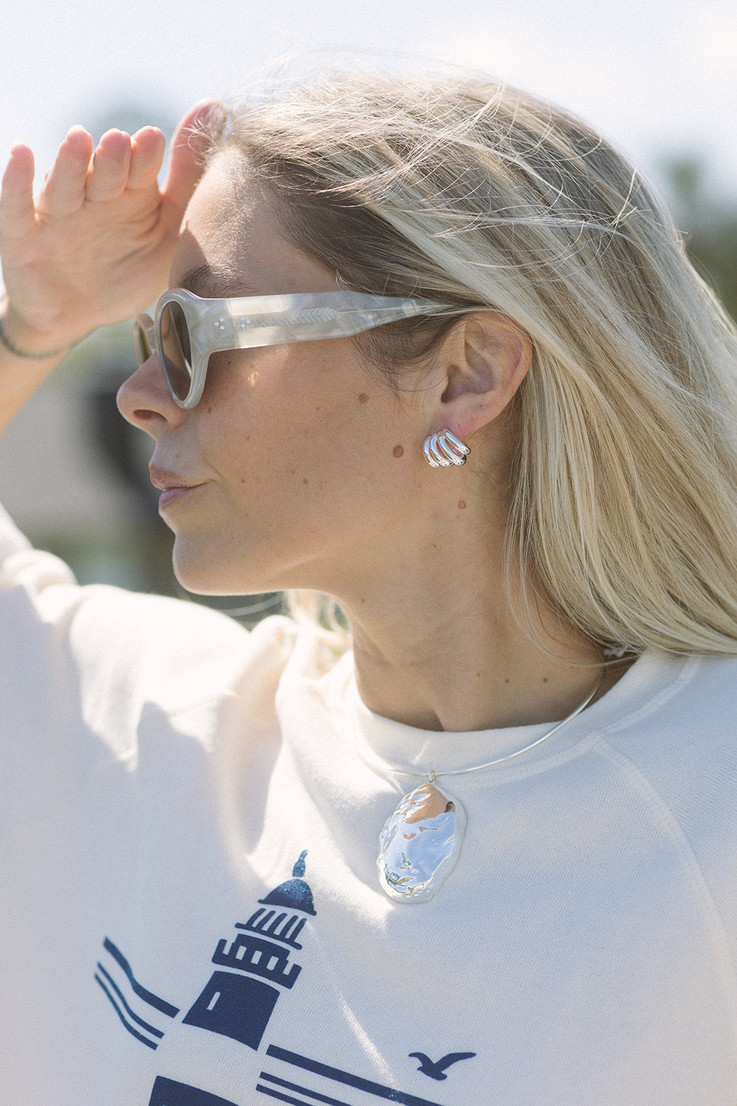 Woman wearing sunglasses and a white shirt with a lighthouse design.