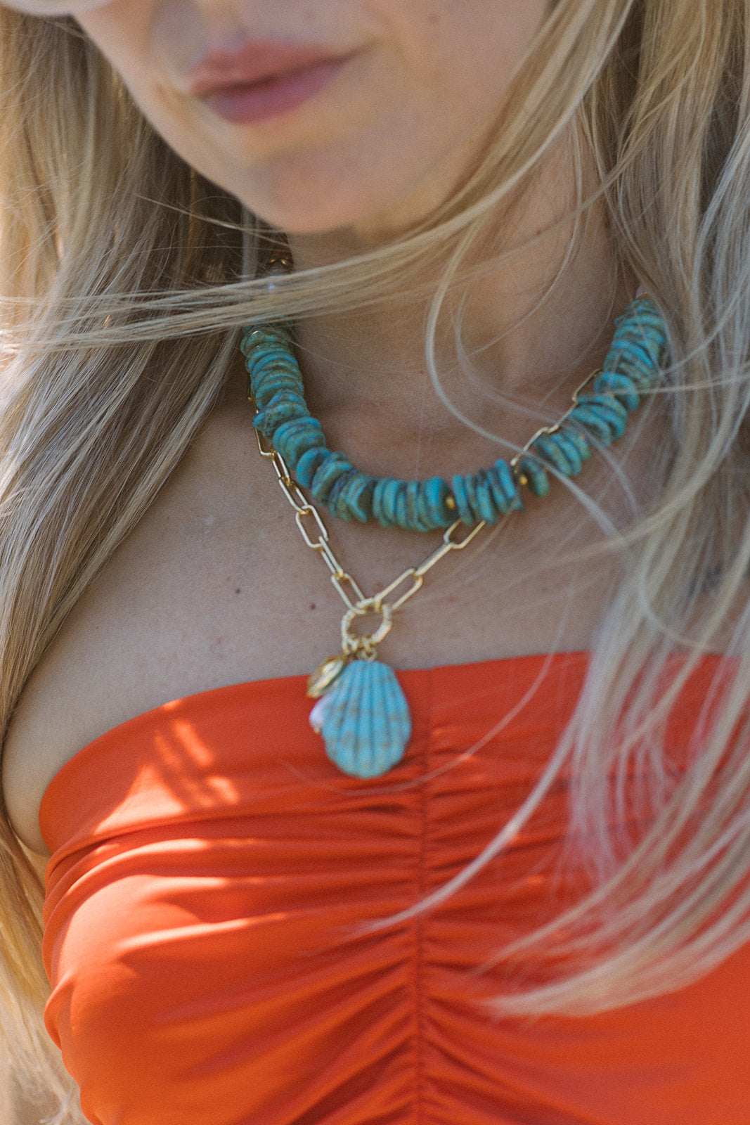 Close-up of a person wearing a turquoise beaded necklace with a shell pendant necklace