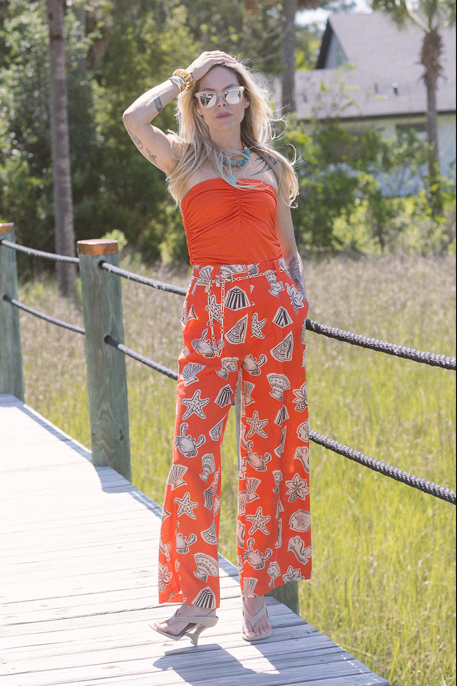Woman in an orange outfit with a pattern standing on a wooden bridge in a natural setting