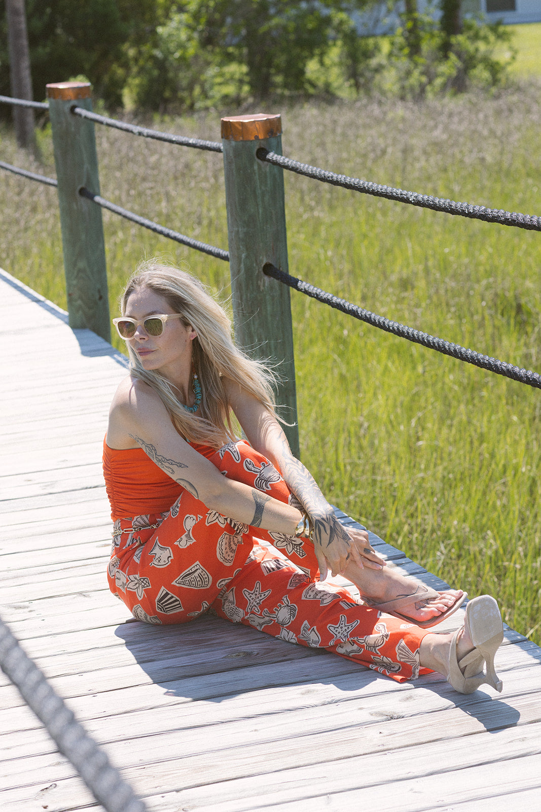 Woman in Bloo Linen Pant sitting on a wooden dock by a grassy area