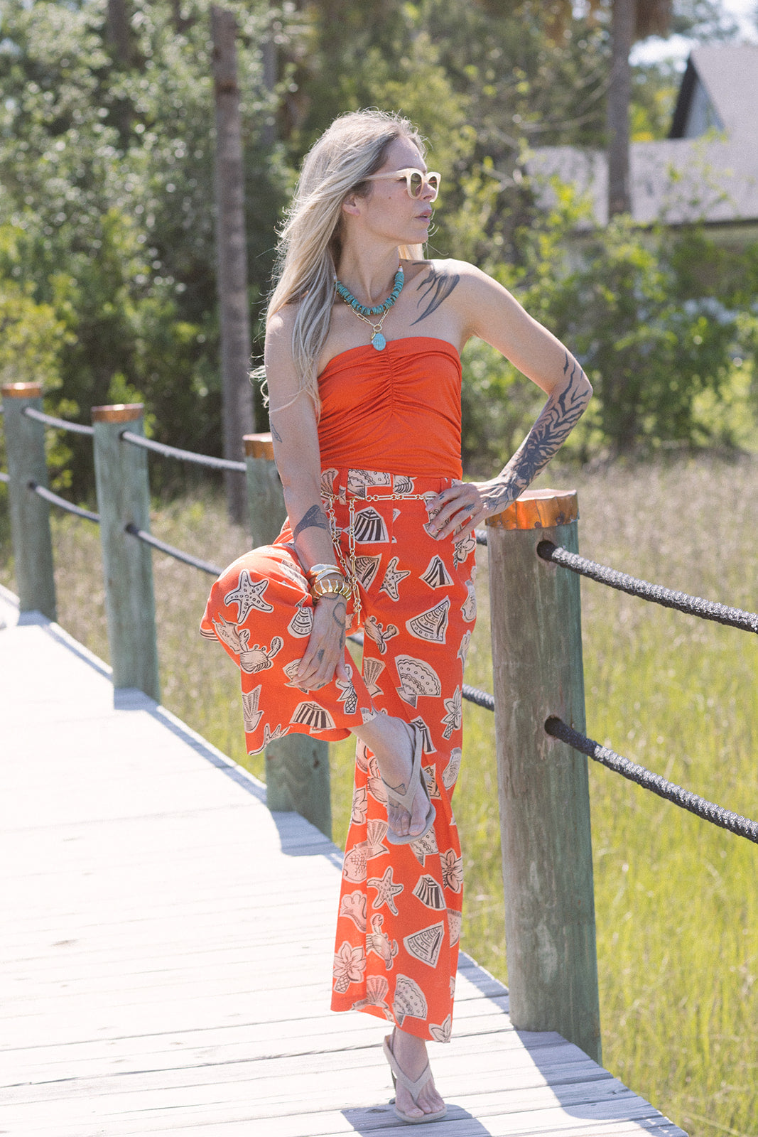 Woman in an orange outfit standing on a wooden bridge with greenery in the background