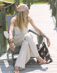 Woman in a beige outfit sitting on a wooden deck with a black and white crochet bag.