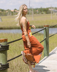 Woman in an orange dress and Monogram Suede Flat Slide standing on a wooden dock with grassy fields and water in the background.
