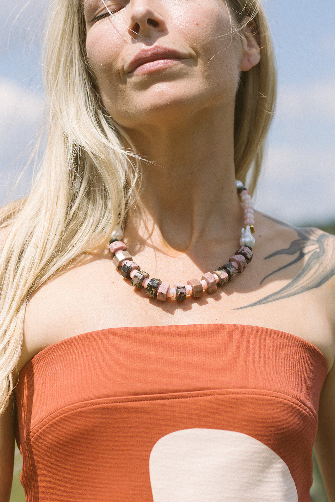 Woman wearing a strapless orange dress and a beaded necklace with a clear sky background