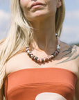 Woman wearing a strapless orange dress and a beaded necklace with a clear sky background