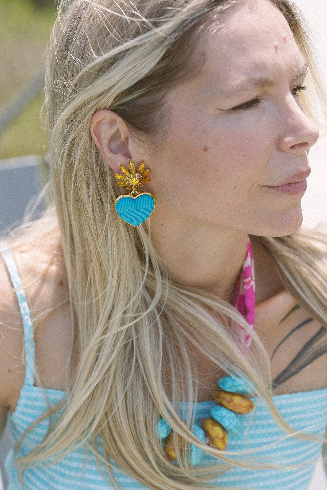 Woman wearing a blue heart-shaped earring with a yellow flower design.