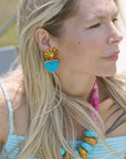 Woman wearing a blue heart-shaped earring with a yellow flower design.