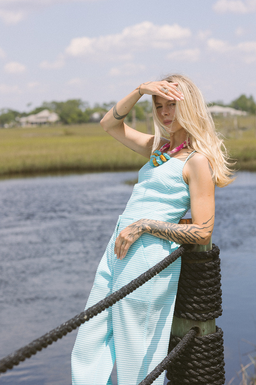 Woman in a blue matching set standing by a body of water with a rope railing.