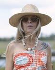 Woman wearing a straw hat and sunglasses with a patterned dress outdoors. Neckline detail