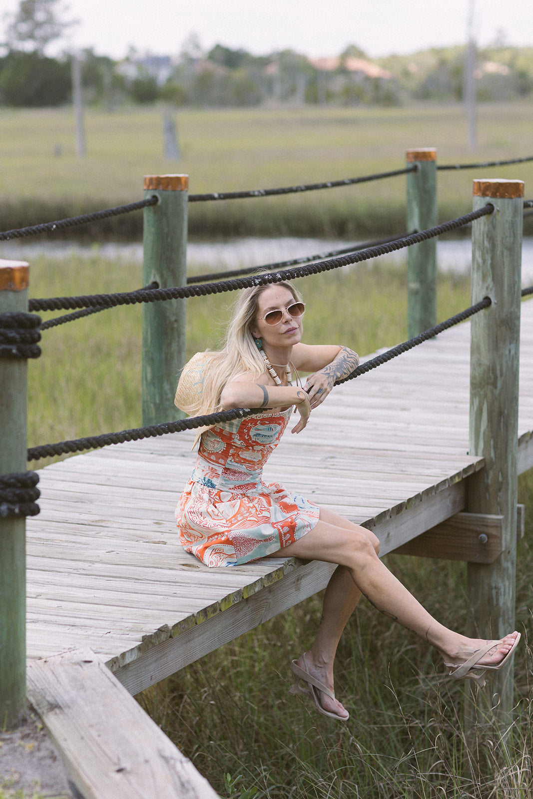 Woman in a colorful dress sitting on a wooden bridge over a marshy area.
