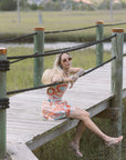 Woman in a colorful dress sitting on a wooden bridge over a marshy area.
